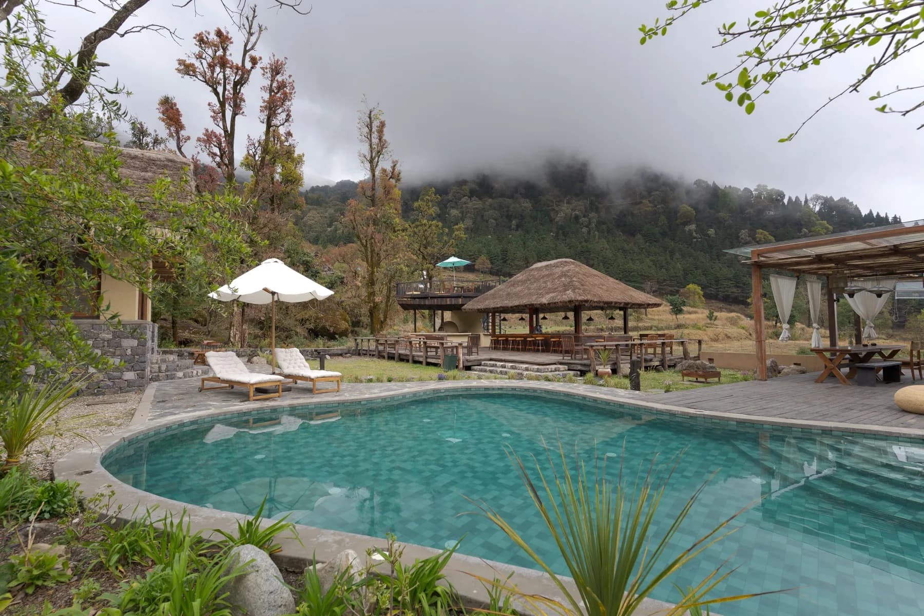 Daytime pool with thatched bar pavilion and misty mountain backdrop at Kaansya