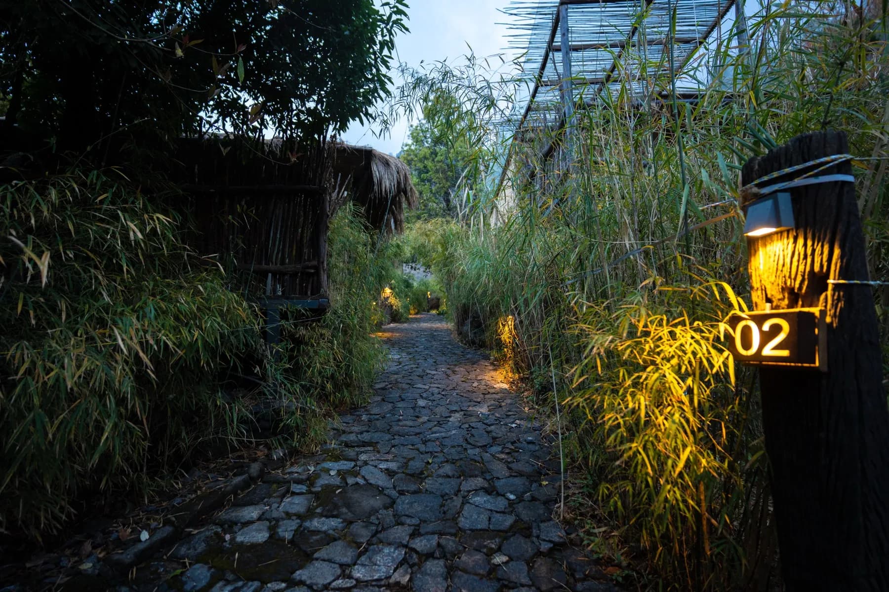Lit cobbled walkway through bamboo to cottage 02 at dusk